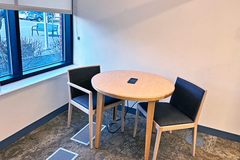 Small study room showing a round table with power adapter built into the top, with two padded chairs. There is a window showing the room is on the first floor.