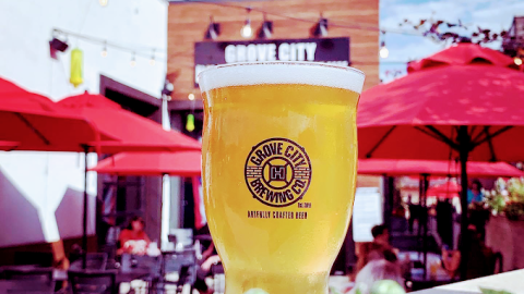 Beer glass with Grove City Brewing Company Logo visible in the foreground while the Grove City Brewing Co.'s patio and restaurant is visible in the background.