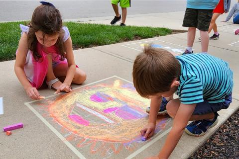 Children on sidewalk drawing the sun with chalk