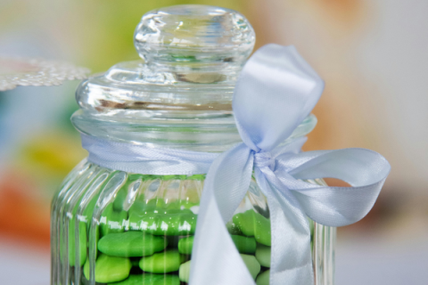 Green candies in a clear glass jar with a white ribbon around it