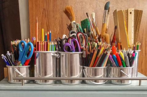 art supplies such as colored pencils, markers, rulers, scissors, and paint brushes stored upright in silver containers