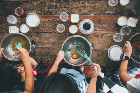 a view from above of children whisking eggs and other ingredients in stainless mixing bowls