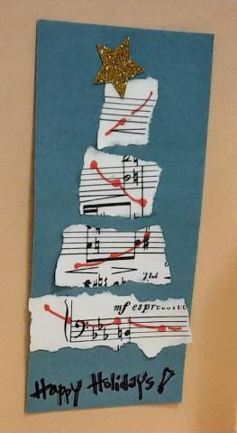 a handmade holiday card with a conifer shaped tree made from torn music paper strips on front of card. Handwritten text on the card reads Happy Holidays