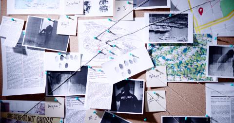 crime investigation board with printouts, photos, notes, and connecting strings pinned to corkboard 