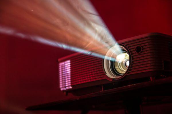 A close-up image of a movie projector with the light streaming out of the lens towards an unseen screen